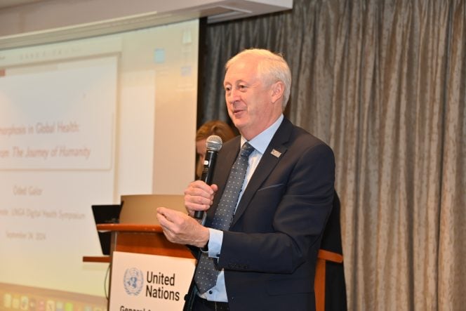 Man in a black suit holding a microphone stands before a slide presentation