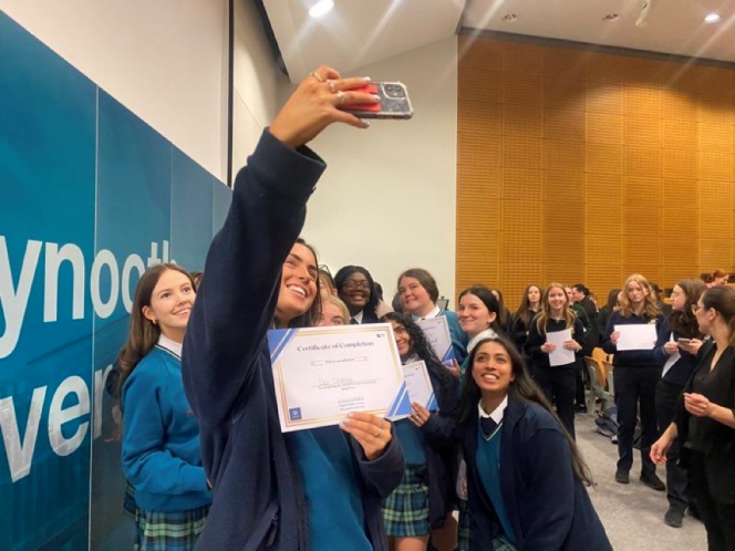 Lots of girls in student uniforms holding certificates taking a selfie on a phone