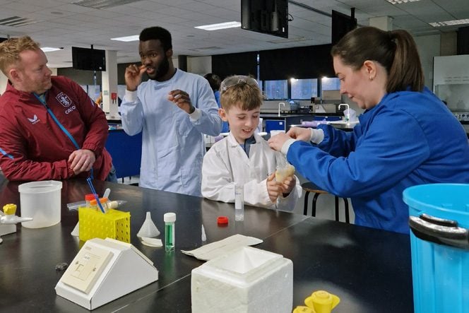 Two men chatting and a woman showing a child beakers in a lab environment