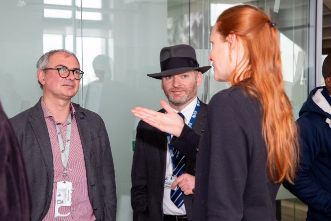 2 men and a woman chatting. Woman's back to the camera