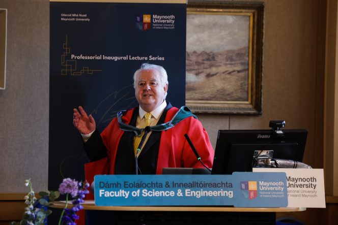Man in a red robe speaking as he stands in front of a blue pop-up banner