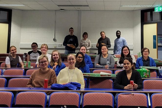 A group of people sitting in a lecture hall eating pizza