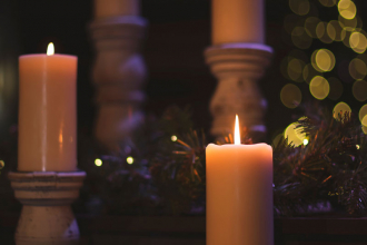 Lit candles against a soft, dark background of pine branches and twinkly lights