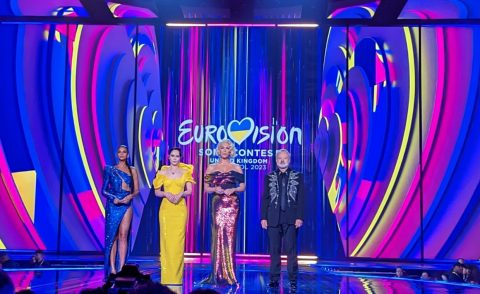 Purple pink and yellow Eurovision 2023 background with three women and a man standing in front of it