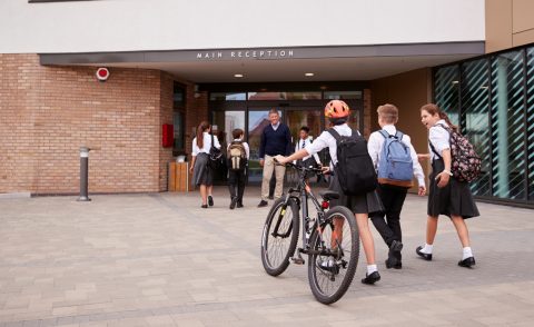 Girl wearing an orange helmet pushing her bike toward school along with two others