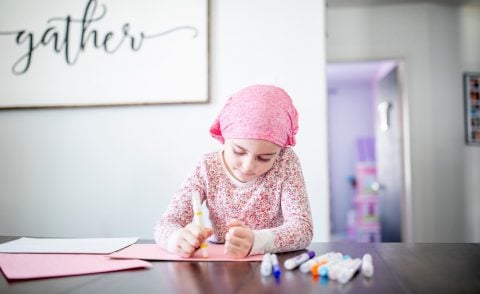 Little girl wearing a pink headscarf sitting at a table drawing with magic markers