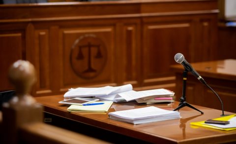 Timber panelled court room with a desk with papers and microphones and symbol of justice in the background