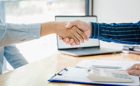 Woman in a blue shirt and man in a striped navy shirt shaking hands across a desk