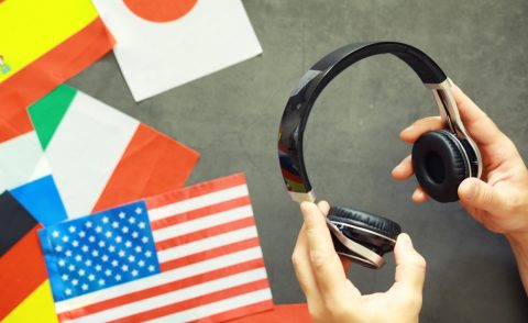 Hands holding headphones against a backdrop of world flags including US, Irish and Japanese flags