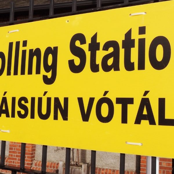 Large yellow sign hanging on railings outside a building that reads: Polling station/Stáisiún Vótála