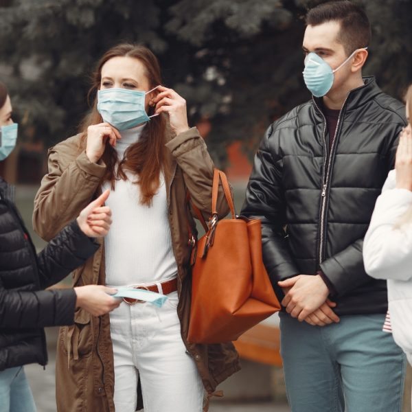 3 women and 1 man talking to each other wearing covid masks. Black jackets. blue jeans, white jacket and brown jacket 