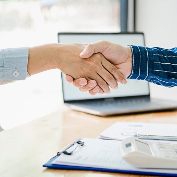 Woman in a blue shirt and man in a striped navy shirt shaking hands across a desk
