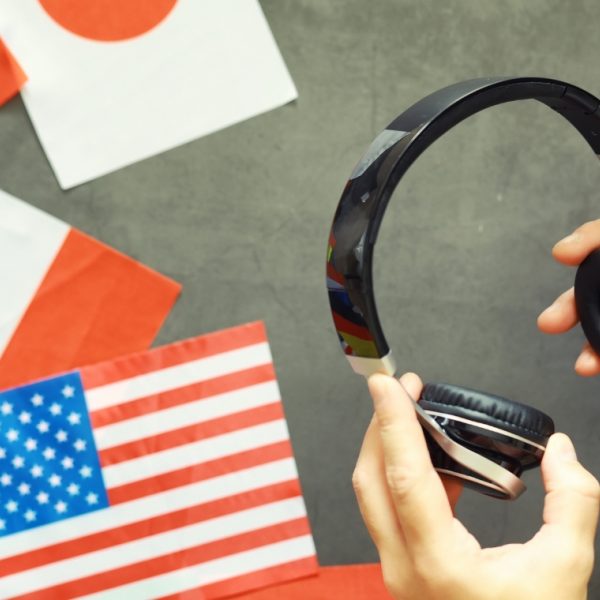 Hands holding headphones against a backdrop of world flags including US, Irish and Japanese flags