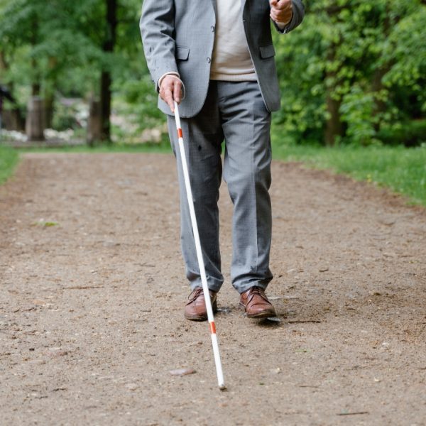 Man in a grey suit with a white cane walking through a park