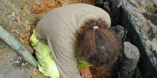 Female archaeologists excavating an object in a hole