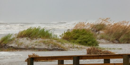 Stormy waves with sand dune grasses blowing in the wind behind a submerged fence