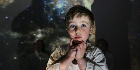 small boy with blue eyes surrounded by projection of space and stars