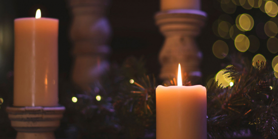 Lit candles against a soft, dark background of pine branches and twinkly lights