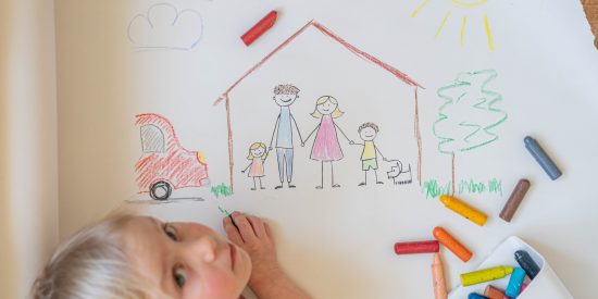 blonde hair child using crayons to draw house, with family and car