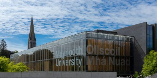 Glass-fronted Maynooth University library building with spire in the background