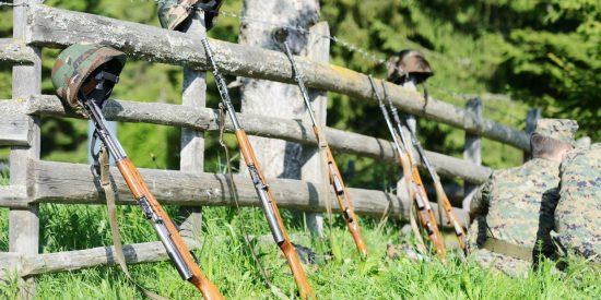 Field with a fence and five guns and three soldiers' helmets proppped against it