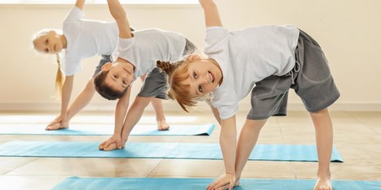 Three children -- two girls and a boy -- standing on blue yoga mats doing triangle poses
