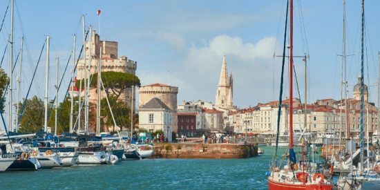 Sunny harbour filled with boats with a historic fortified building in the background