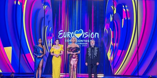 Purple pink and yellow Eurovision 2023 background with three women and a man standing in front of it