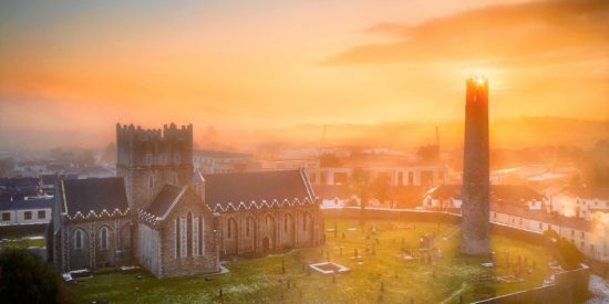 Medieval cathedral sitting in a wall graveyard containing a round tower in sunlight