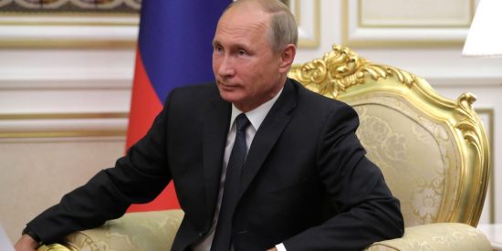 Russian President Valdimir Putin seated on a large gold chair with Russian flag in the background