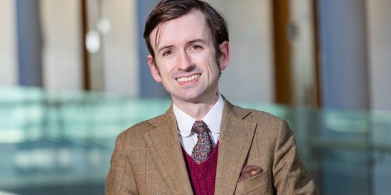 Smiling young man in a brown tweed jacket and red vest 