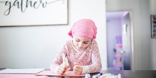 Little girl wearing a pink headscarf sitting at a table drawing with magic markers