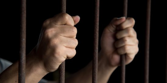 Man's hands gripping prison bars