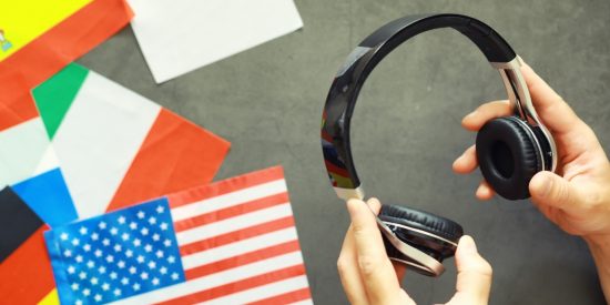 Hands holding headphones against a backdrop of world flags including US, Irish and Japanese flags