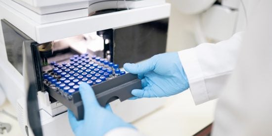 Person wearing blue gloves inserting a tray of vials into a spectrometer