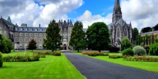 Green quadrangle with trees and flower beds with a grey building and a church with spire in the background
