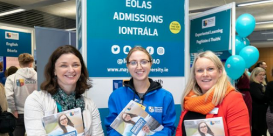 Two Admissions Office staff with a student ambassador holding prospectuses at open day stand