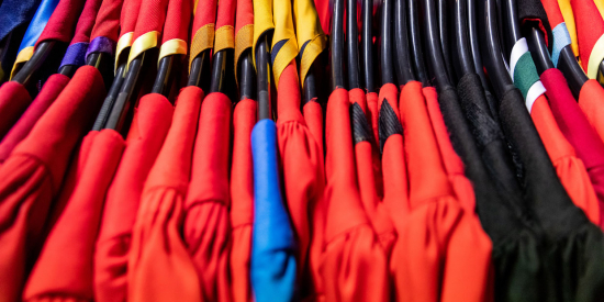 Doctoral conferring robes, a mix of red blue and black, hanging up on a clothes rack with their coloured shawls