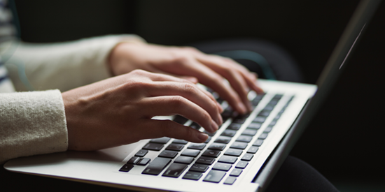 Hands type on a silver laptop keyboard against a dark background