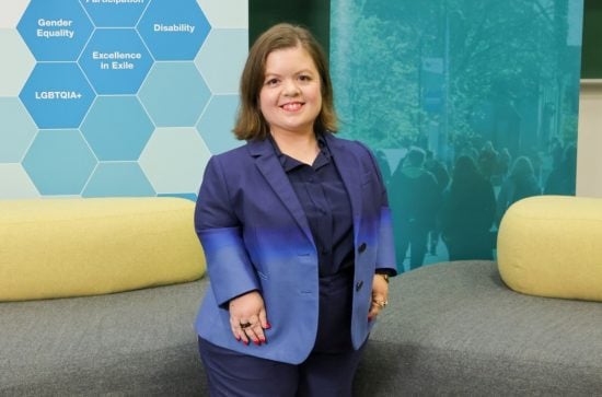 Sinéad Burke stands in front of seating and backdrops at the Equitas Conference.  Sinead is wearing an incredible blazer with a blue into navy gradient 