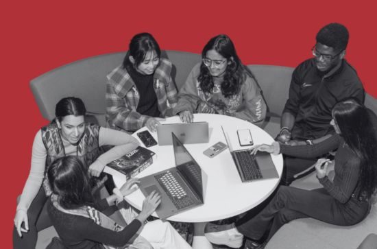 Students sat at a table chatting with each other, red background.