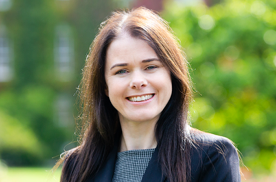 A portrait of Karen Lynch Shally in a navy blazer. Karen is looking to camera, St Josephs Square is in the background