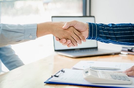 Woman in a blue shirt and man in a striped navy shirt shaking hands across a desk
