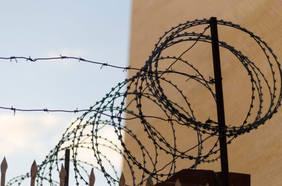 Roll of barbed wire on a wall between a brown wall and a blue sky