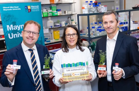 Two men and a woman in a white coat holding a rack of test tubes in a laboratory