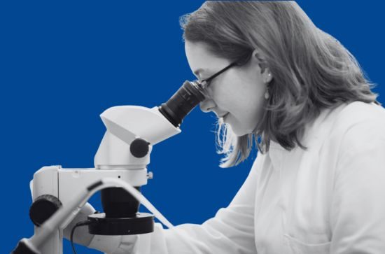 Student viewing a specimen through a microscope, dark blue background.
