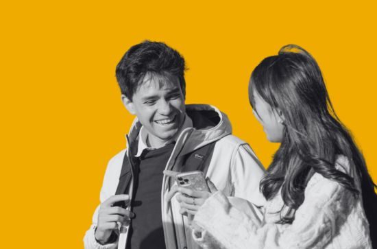 Two students walking and talking, yellow background.